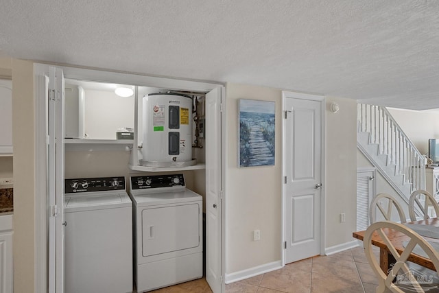 laundry room with water heater, cabinets, washer and clothes dryer, light tile patterned floors, and a textured ceiling