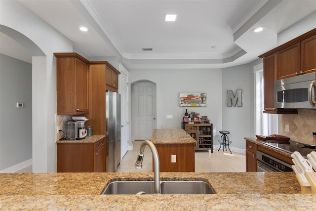 kitchen featuring appliances with stainless steel finishes, arched walkways, a sink, and light stone counters