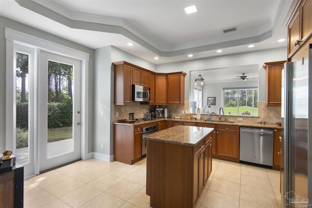 kitchen featuring stainless steel appliances, a sink, ornamental molding, dark stone counters, and a raised ceiling