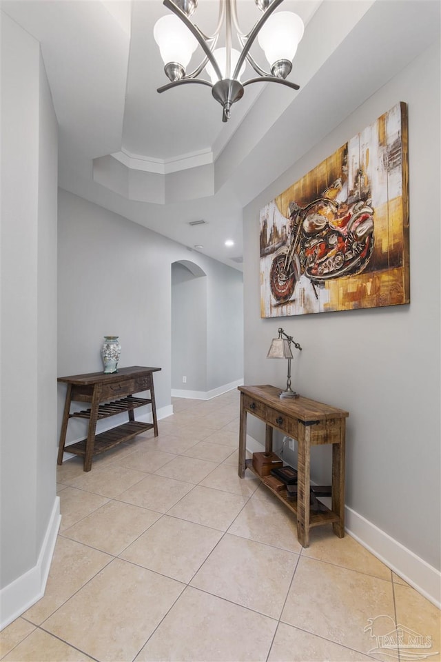 hall with arched walkways, light tile patterned flooring, baseboards, a tray ceiling, and an inviting chandelier