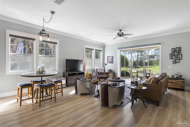 living room with ornamental molding, light wood-style flooring, baseboards, and a ceiling fan