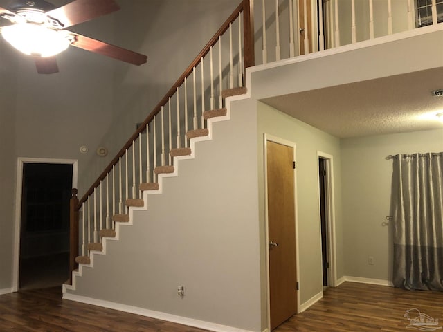 stairs with ceiling fan, a high ceiling, baseboards, and wood finished floors