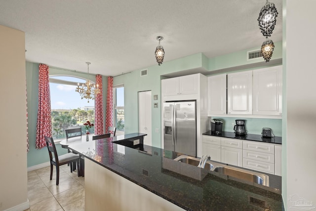 kitchen featuring stainless steel refrigerator with ice dispenser, sink, dark stone countertops, white cabinets, and hanging light fixtures