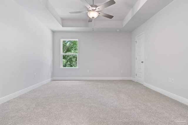 empty room with ceiling fan, a tray ceiling, and light colored carpet