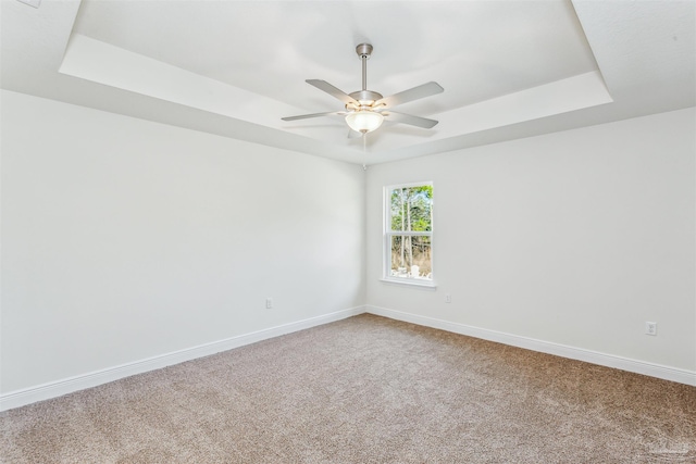 empty room with carpet floors, a tray ceiling, baseboards, and a ceiling fan