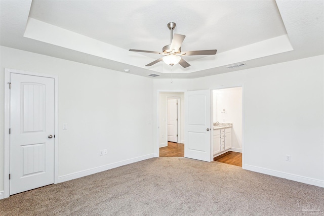 unfurnished bedroom featuring visible vents, a tray ceiling, baseboards, and light colored carpet