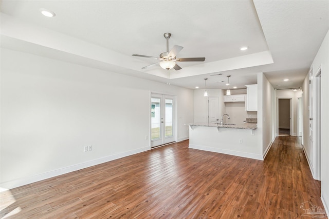 interior space featuring recessed lighting, wood finished floors, a ceiling fan, baseboards, and a tray ceiling