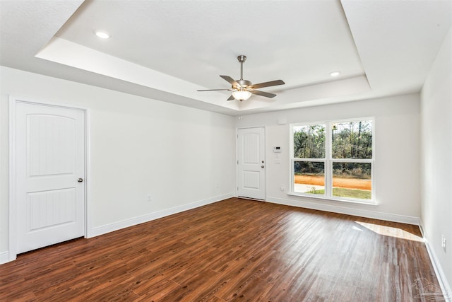 spare room featuring a tray ceiling, dark wood finished floors, and baseboards