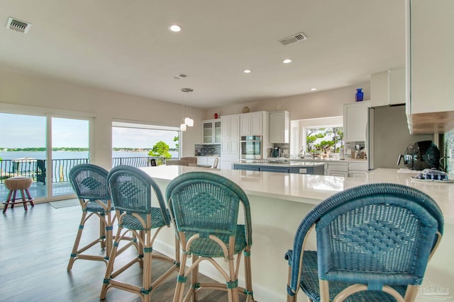 kitchen with hanging light fixtures, stainless steel appliances, a water view, white cabinets, and light wood-type flooring