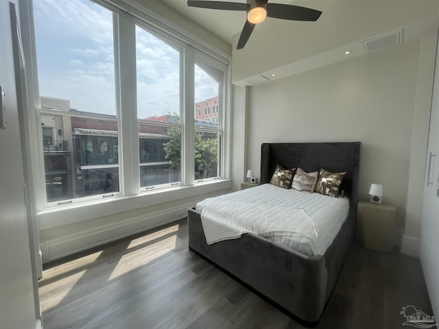 bedroom with a ceiling fan, visible vents, baseboards, and wood finished floors