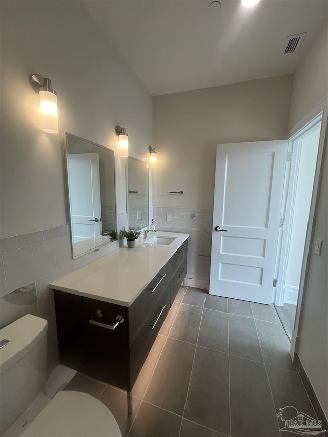 bathroom with toilet, tile patterned flooring, tile walls, and vanity