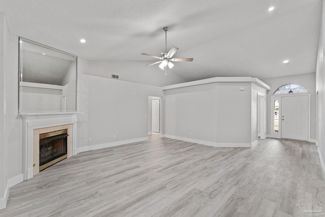 unfurnished living room featuring a textured ceiling, ceiling fan, a fireplace, light hardwood / wood-style floors, and lofted ceiling