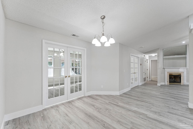 unfurnished dining area featuring french doors, an inviting chandelier, lofted ceiling, a textured ceiling, and light wood-type flooring