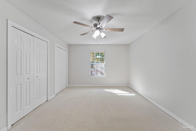 unfurnished bedroom featuring ceiling fan, light colored carpet, a textured ceiling, and two closets