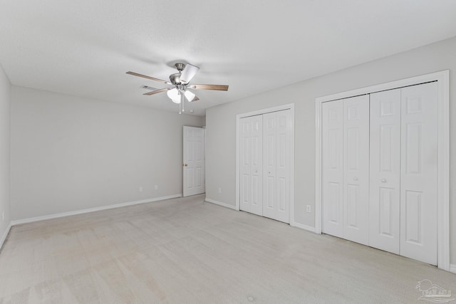 unfurnished bedroom with ceiling fan, light carpet, and multiple closets