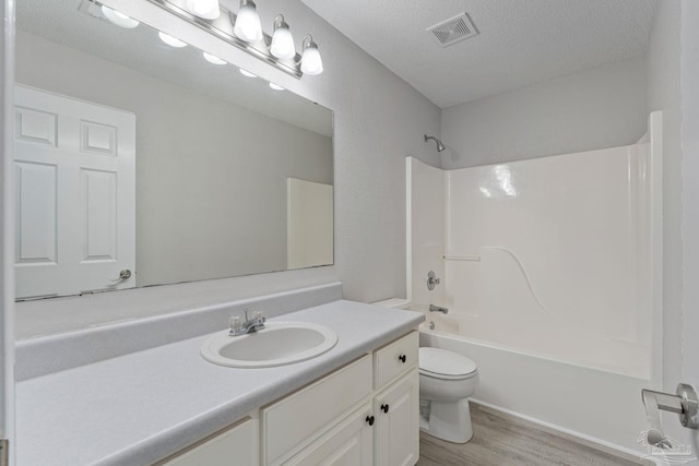 full bathroom with hardwood / wood-style floors, a textured ceiling, toilet, vanity, and bathtub / shower combination