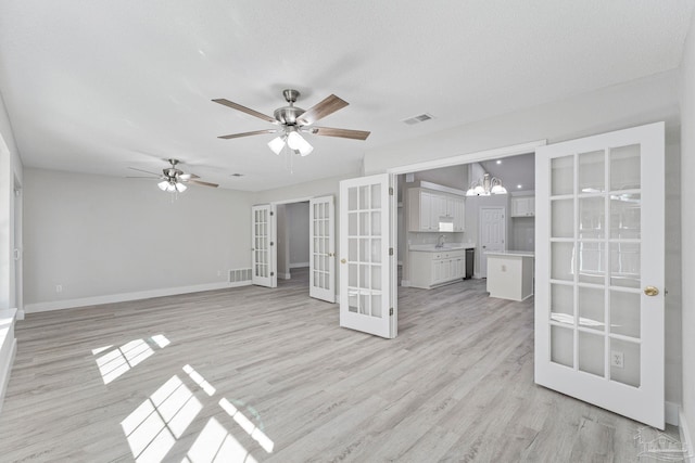 unfurnished living room featuring french doors, light wood-type flooring, ceiling fan with notable chandelier, a textured ceiling, and vaulted ceiling