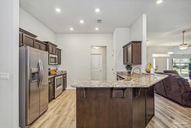 kitchen featuring light hardwood / wood-style floors, kitchen peninsula, stainless steel appliances, a kitchen bar, and ceiling fan