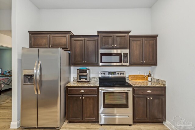 kitchen featuring dark brown cabinetry, light stone countertops, stainless steel appliances, and light hardwood / wood-style floors