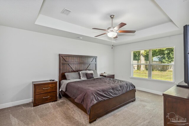 bedroom featuring light carpet, ceiling fan, and a raised ceiling