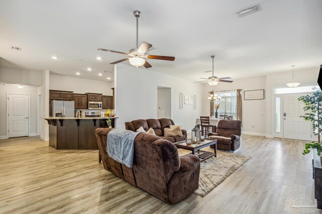 living room featuring ceiling fan with notable chandelier and light hardwood / wood-style floors