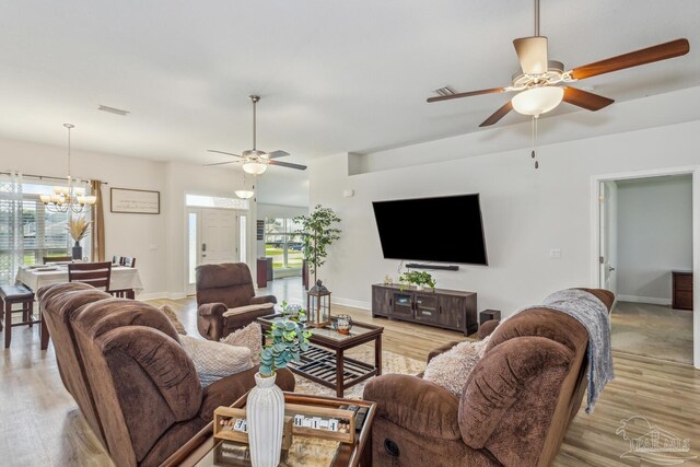 living room with ceiling fan with notable chandelier and light hardwood / wood-style floors