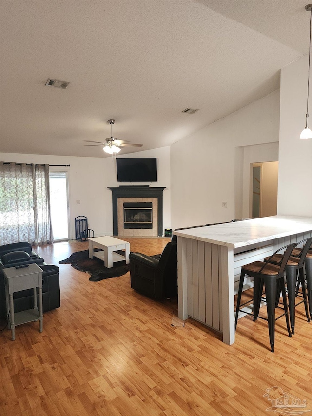 living room with a tiled fireplace, ceiling fan, lofted ceiling, and light wood-type flooring