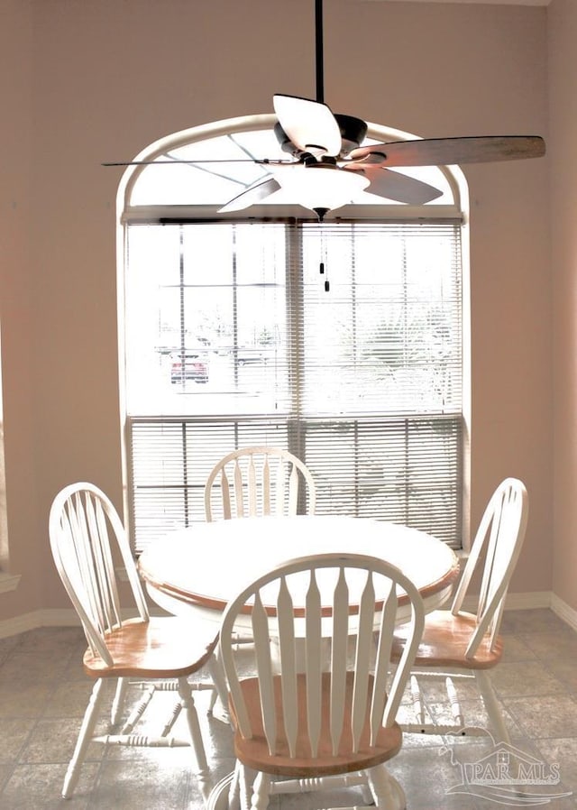 dining space with stone tile floors, a ceiling fan, and baseboards