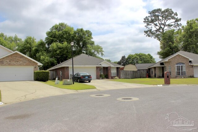 view of front of home featuring a front lawn, driveway, fence, brick siding, and a garage