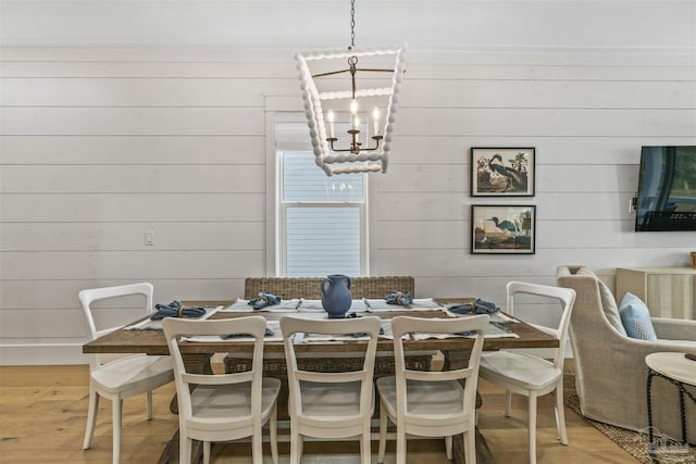 dining space with wooden walls, light hardwood / wood-style floors, and an inviting chandelier