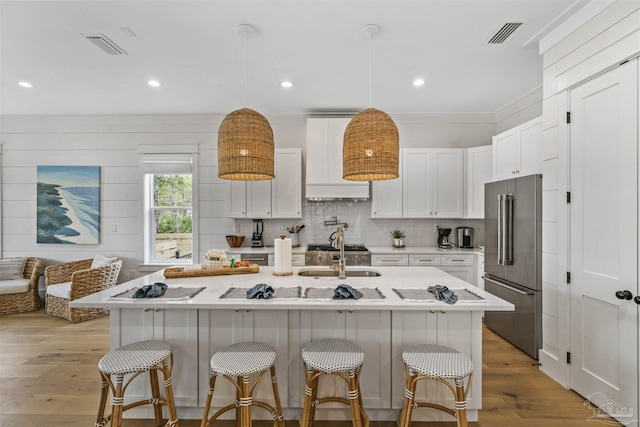 kitchen featuring high end refrigerator, a kitchen island with sink, sink, light hardwood / wood-style floors, and white cabinetry