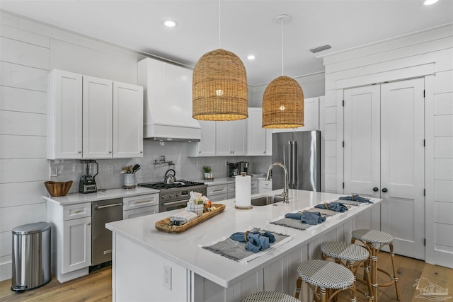 kitchen with a kitchen island with sink, sink, decorative light fixtures, high quality appliances, and white cabinets