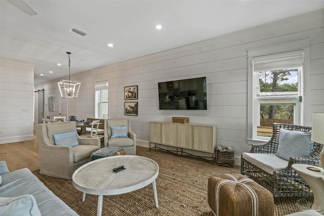 living room featuring a barn door, wood walls, dark wood-type flooring, and an inviting chandelier