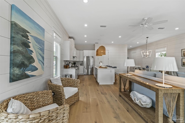 living room with sink, ceiling fan with notable chandelier, light hardwood / wood-style flooring, and wood walls