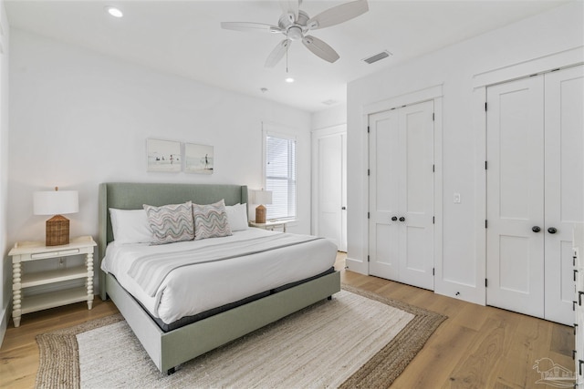 bedroom featuring hardwood / wood-style floors, ceiling fan, and multiple closets