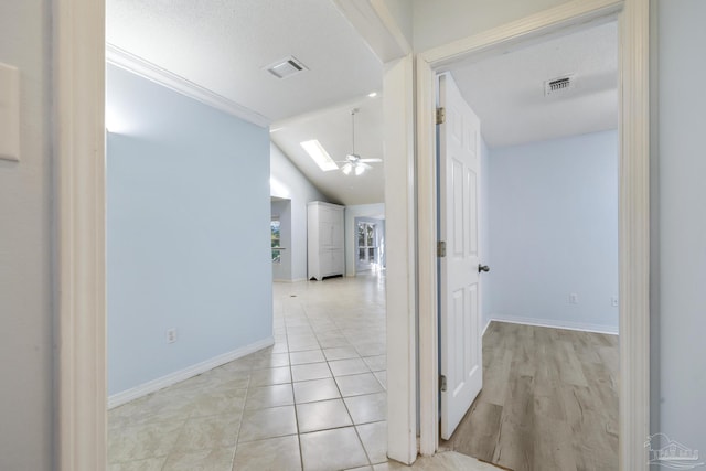 corridor with light tile patterned floors, a textured ceiling, lofted ceiling with skylight, and ornamental molding