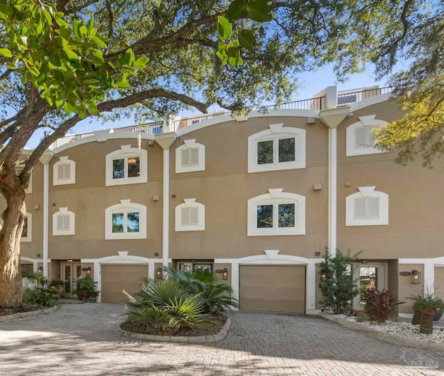 multi unit property featuring stucco siding, decorative driveway, and a garage