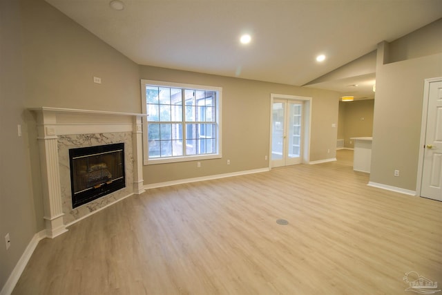 unfurnished living room featuring light hardwood / wood-style floors, vaulted ceiling, a fireplace, and french doors