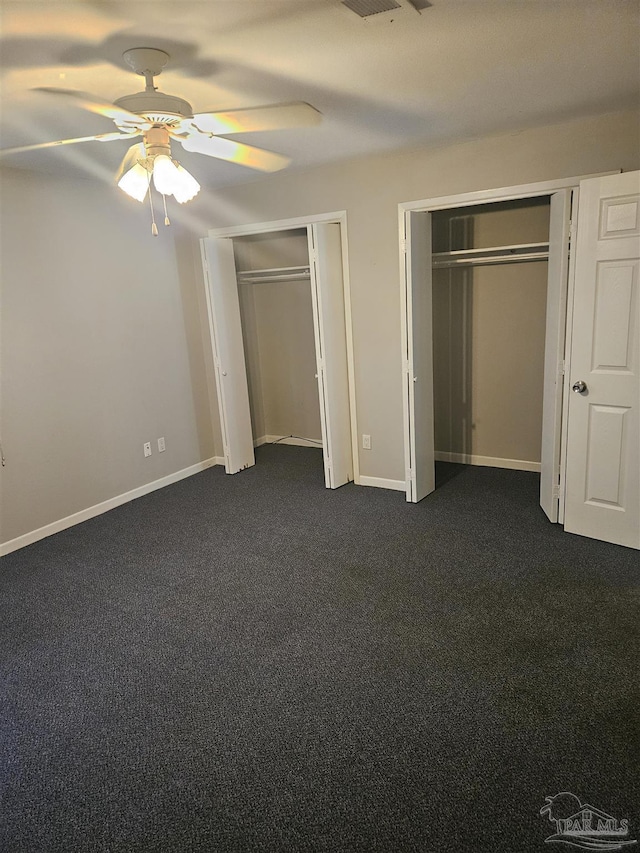 unfurnished bedroom featuring baseboards, multiple closets, dark carpet, and ceiling fan