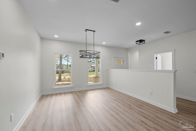 unfurnished dining area with a notable chandelier and light wood-type flooring