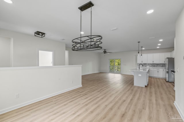 kitchen featuring a kitchen island with sink, hanging light fixtures, light wood-type flooring, white cabinetry, and ceiling fan with notable chandelier