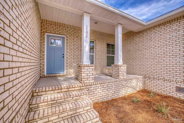 view of exterior entry with covered porch and brick siding