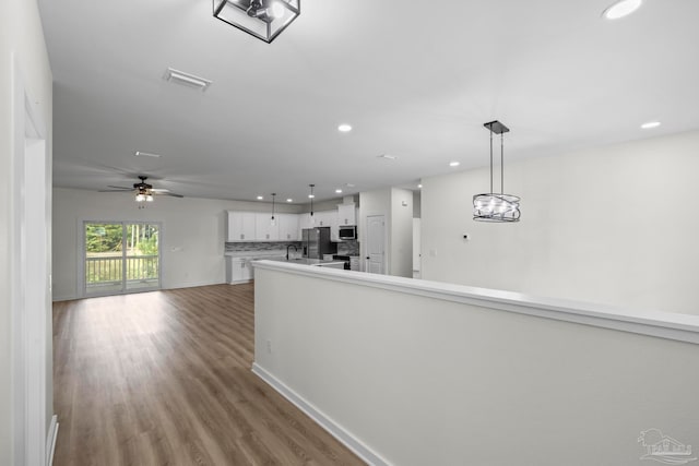 kitchen with ceiling fan with notable chandelier, white cabinetry, stainless steel appliances, pendant lighting, and light hardwood / wood-style flooring