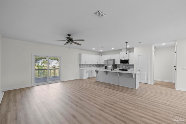 kitchen with white cabinets, tasteful backsplash, a center island with sink, appliances with stainless steel finishes, and light hardwood / wood-style floors