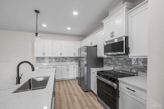 kitchen featuring hanging light fixtures, appliances with stainless steel finishes, white cabinetry, light hardwood / wood-style flooring, and sink