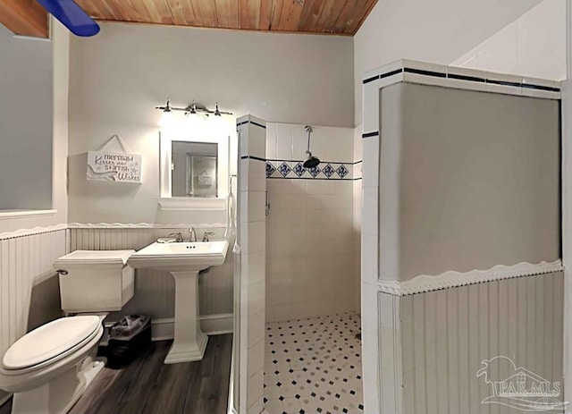 bathroom with wooden ceiling, toilet, wood finished floors, tiled shower, and wainscoting