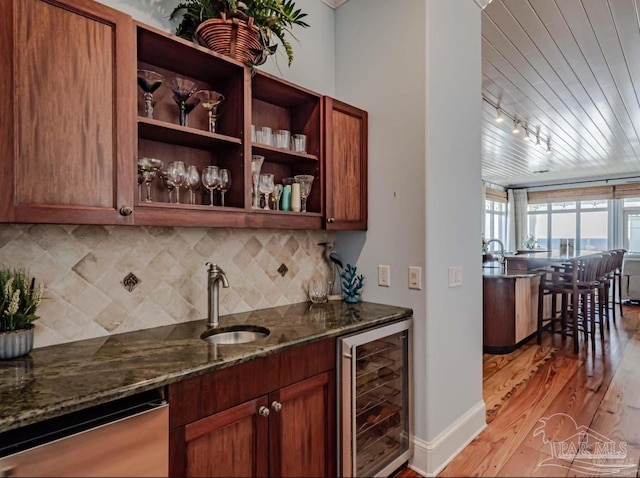 kitchen featuring beverage cooler, dark stone counters, track lighting, and light hardwood / wood-style floors