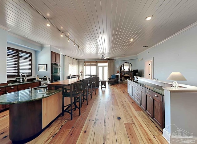 kitchen featuring a large island, light wood finished floors, double oven, a sink, and wooden ceiling