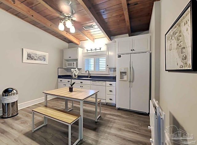 kitchen with white appliances, dark countertops, wooden ceiling, white cabinetry, and a sink