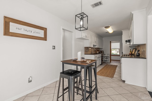 kitchen featuring light tile patterned floors, backsplash, decorative light fixtures, white cabinets, and a breakfast bar area